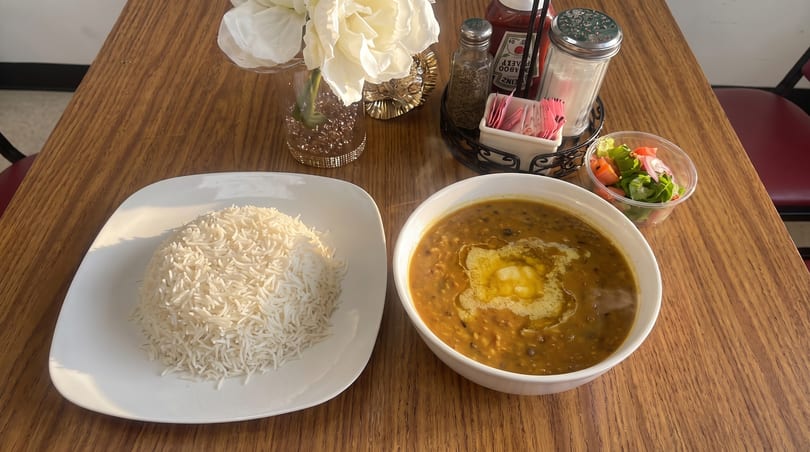 A bowl of dal makhani with butter, a plate of white rice, and a side salad on a wooden table.