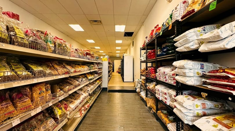 A narrow grocery store aisle with shelves packed with bags of dry goods and food items.