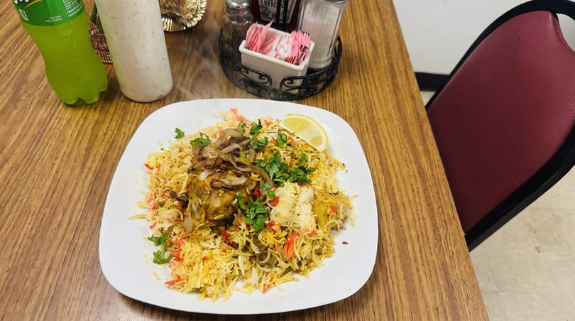 Steaming chicken biryani with fried onions, cilantro, and a lemon wedge on a white plate.
